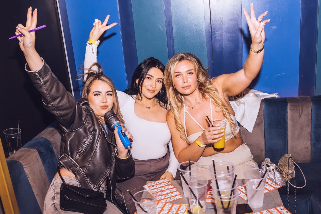 Bingo cards, pop music, festival atmosphere, DJ booth, crowd dancing, prize table, party lights, birthday celebration, event venue, excited attendees, bingo caller, dance floor, interactive games, confetti burst, celebratory moments.